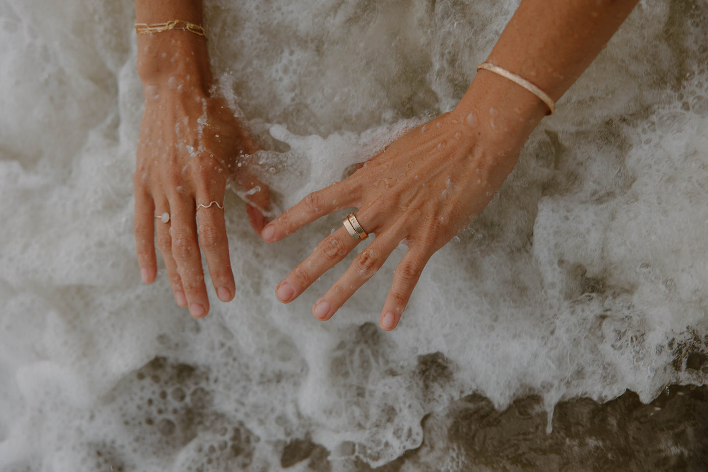 Hands reaching into foamy water with a ring on one finger