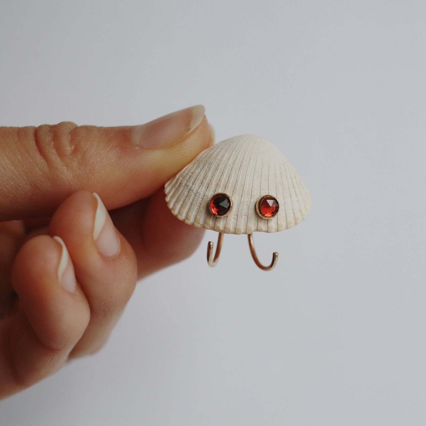 Shell-shaped earring with red gemstones held between fingers against a plain background
